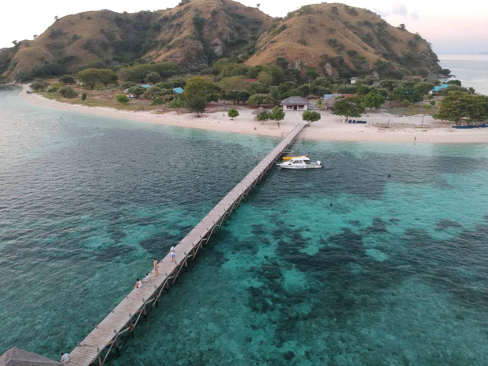 Aerial view of Kanawa Island’s long wooden jetty over clear reef