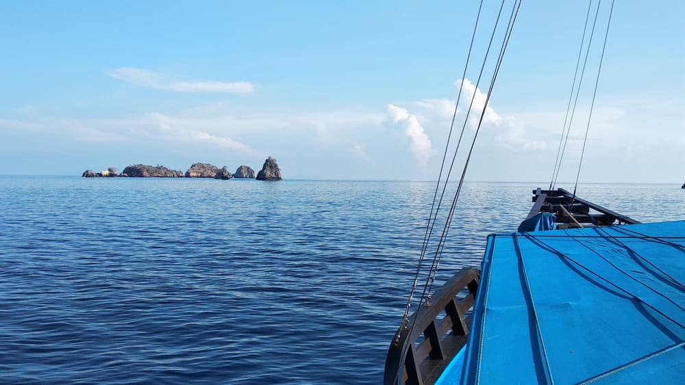 Blue sails and the bow of a boat heading towards rocky islets